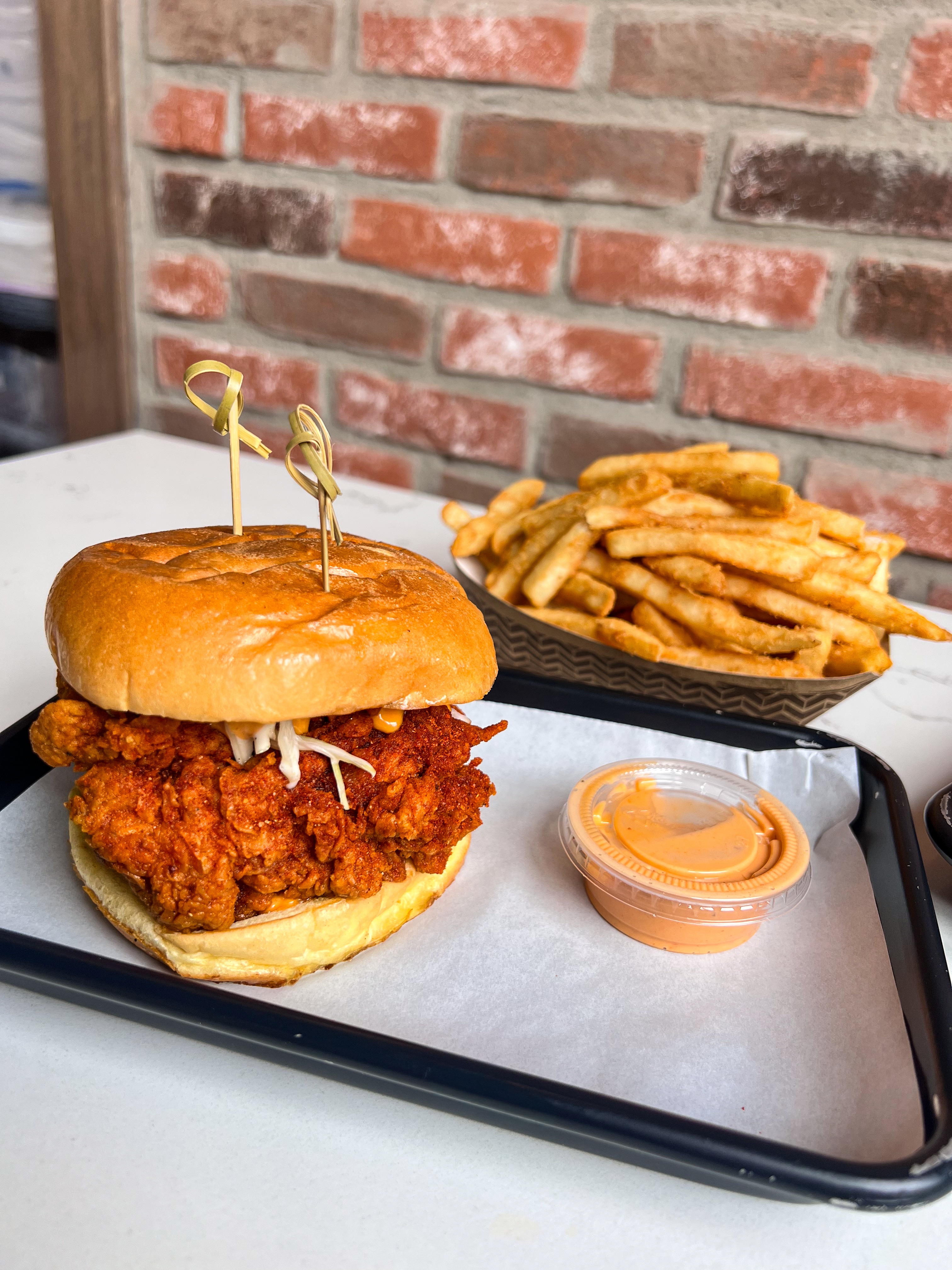 Crispy fried chicken sandwich on a toasted brioche bun with golden French fries and orange dipping sauce