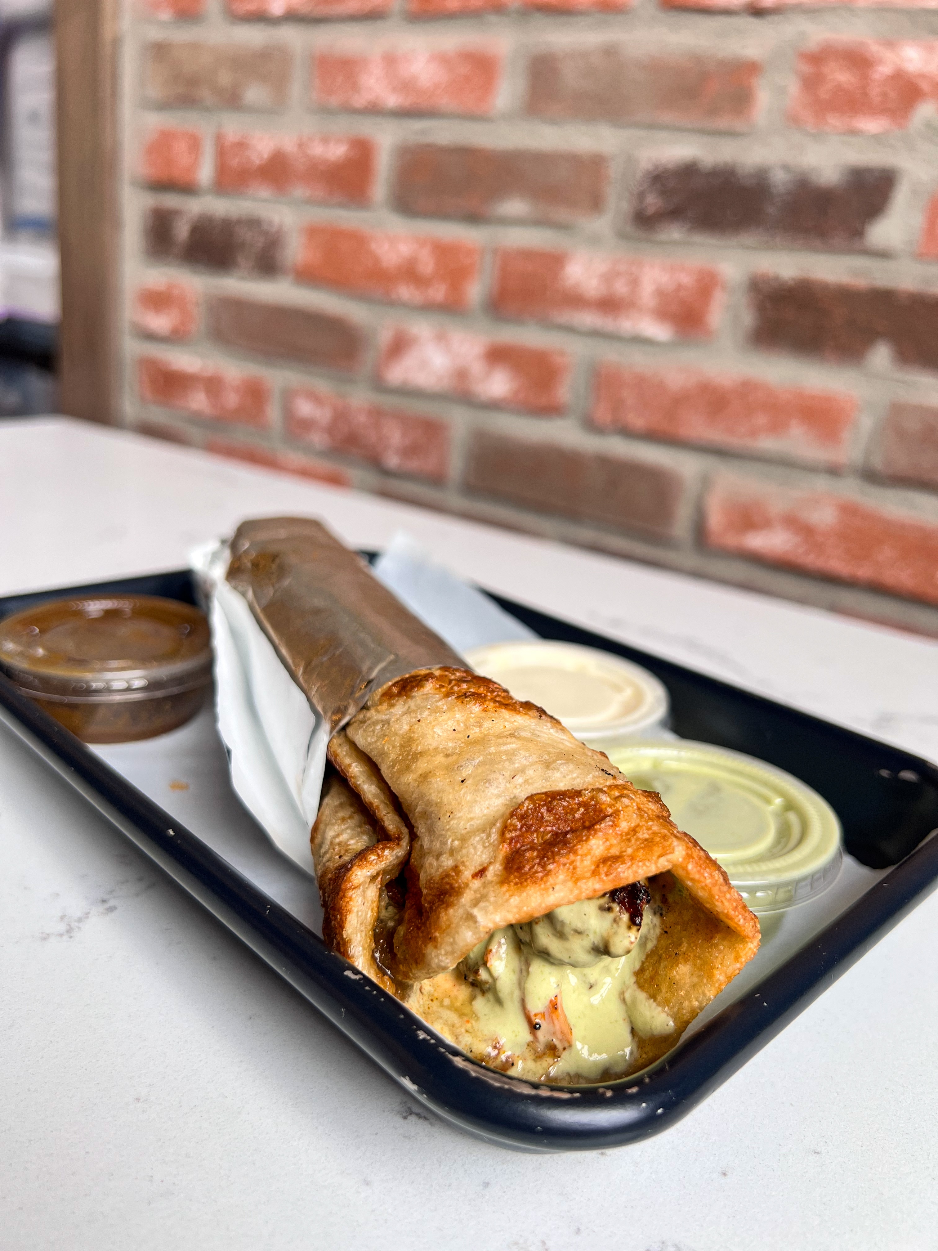 Large golden-brown savory wrap or burrito, sliced in half to reveal fillings, served with sauce and lime wedge