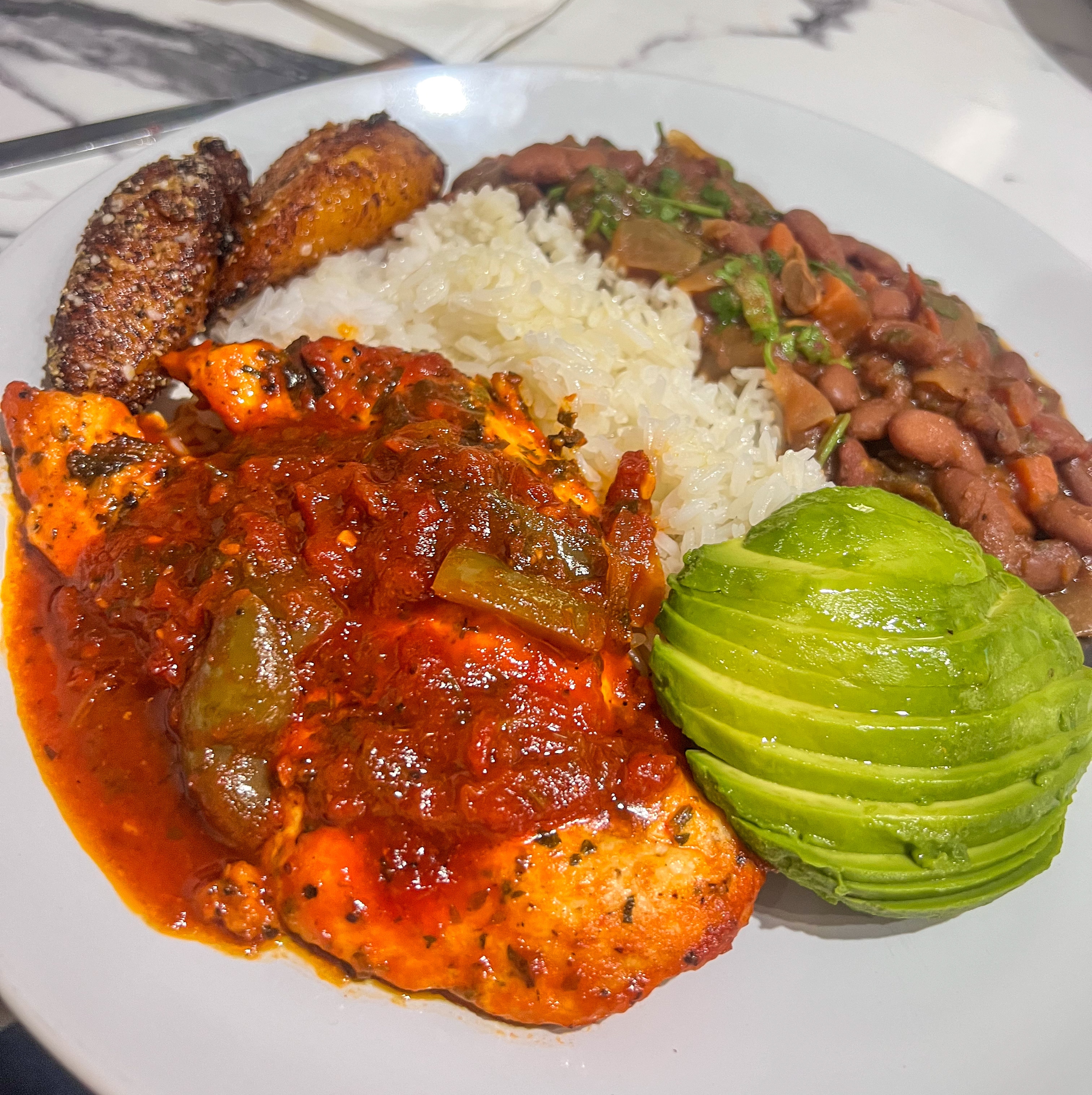 Fish or chicken covered in rich red pepper-based sauce, served with white rice, black beans, avocado, and fried plantains