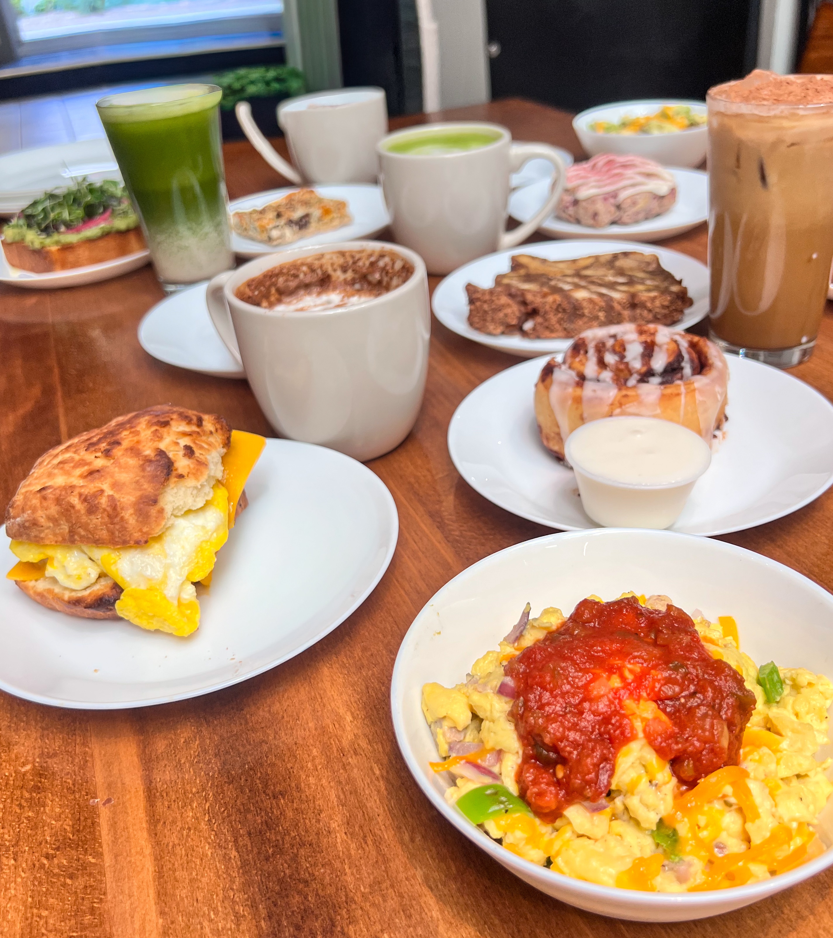 Inviting breakfast spread with croissant sandwich, scrambled eggs, breakfast potatoes, coffee cups, and pastries